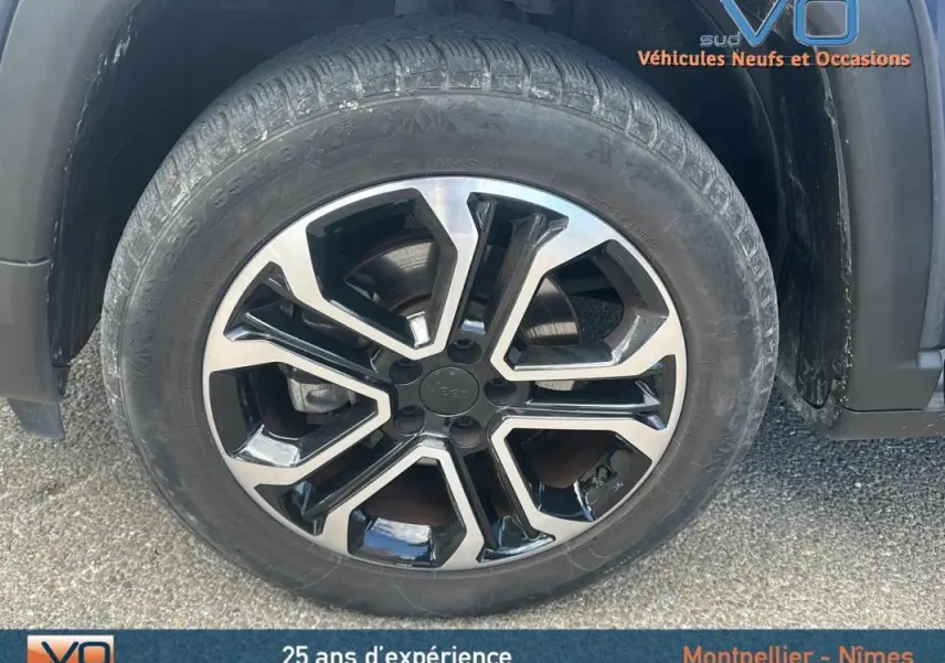 Gros plan sur la jante 18 pouces bicolore du Jeep Compass bleu 2023 avec pneu hiver visible.