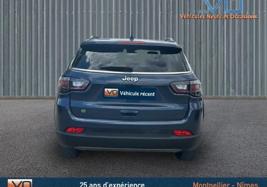 Vue arrière d'un Jeep Compass bleu 2023 avec feux LED et barres de toit visibles sur fond urbain.