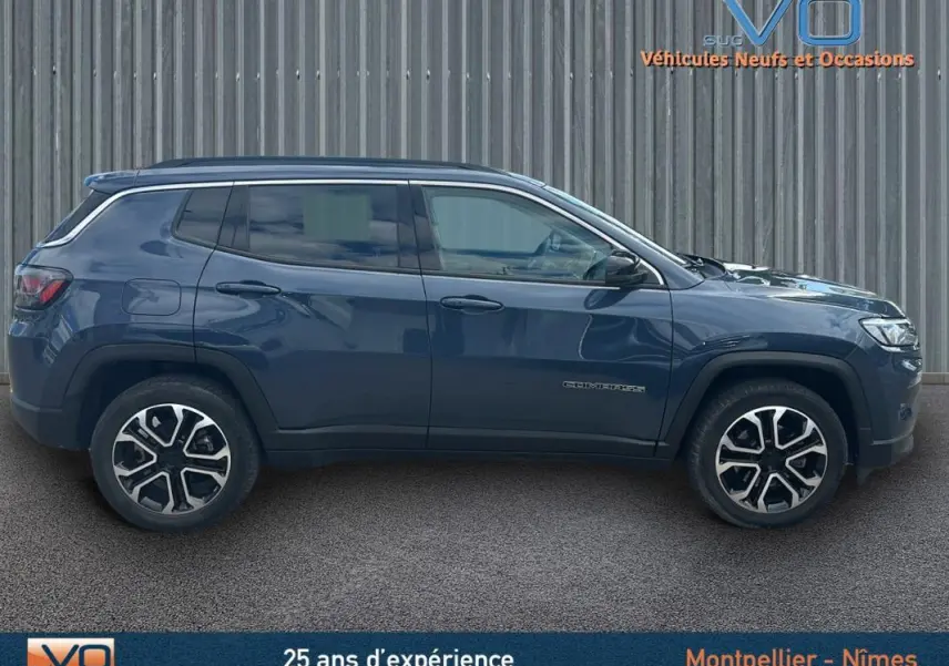 Profil latéral droit d'un Jeep Compass bleu 2023 avec jantes 18 pouces et barres de toit visibles sur fond neutre.