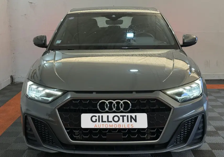 Vue frontale d'une Audi A1 S line gris foncé avec phares LED allumés et calandre hexagonale noire.