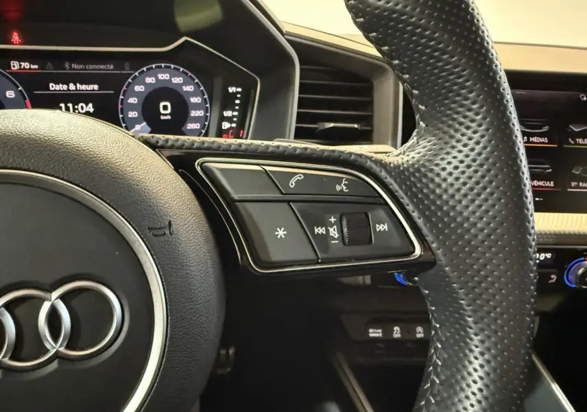 Gros plan sur le volant cuir perforé d'une Audi A1 1.5 TFSI S line 2020 avec tableau de bord digital allumé.