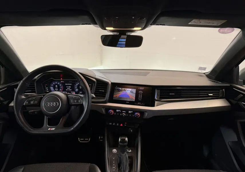 Vue intérieure avant de l'Audi A1 1.5 TFSI S line 2020, tableau de bord gris foncé avec écran digital et volant cuir multifonctions.