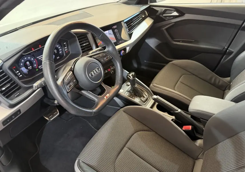 Intérieur Audi A1 2020 vu côté conducteur, volant cuir multifonctions et sièges tissu gris foncé.