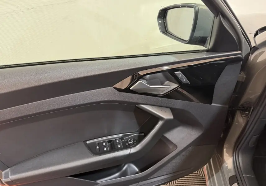 Vue intérieure du panneau de porte côté conducteur gris foncé de l'Audi A1 1.5 TFSI S line avec commandes de vitres et rétroviseur.