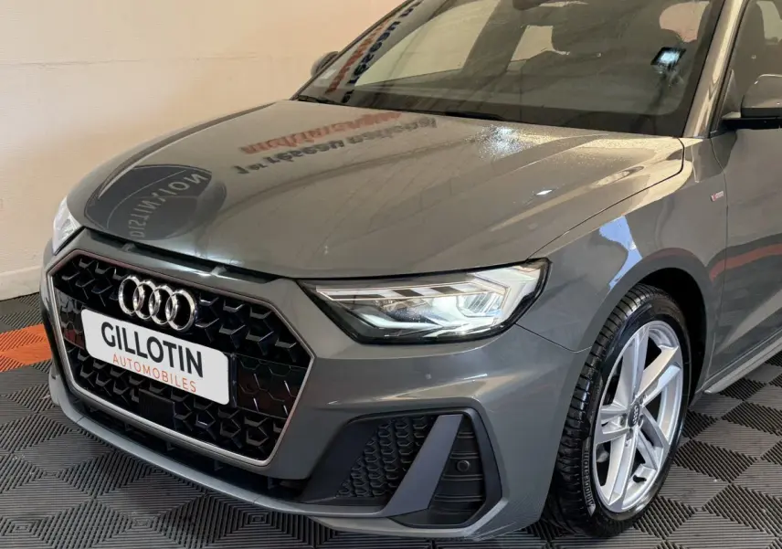 Vue 3/4 avant droit d'une Audi A1 S line gris foncé avec calandre hexagonale et phares LED allumés.