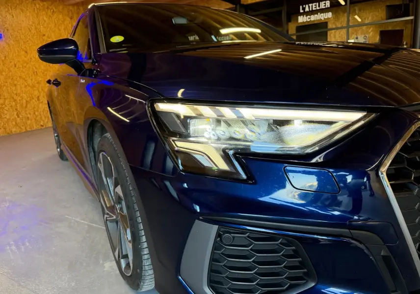 Vue 3/4 avant gauche d'une Audi A3 2.0 TDI S-Line bleu foncé avec phares LED et calandre hexagonale.