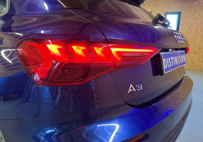 Vue 3/4 arrière droite d'une Audi A3 bleu 2022 avec feux arrière LED allumés et logo A3 visible sur le hayon.