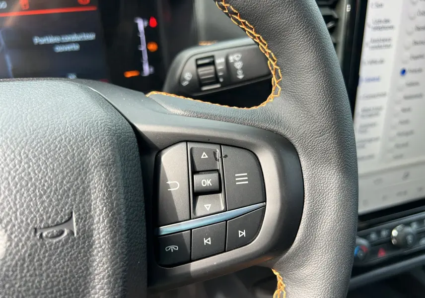 Gros plan sur les commandes multifonctions à droite du volant cuir noir avec surpiqûres orange du Ford Ranger Wildtrak 2025.