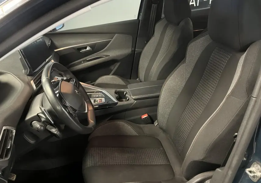 Intérieur côté conducteur du Peugeot 3008 bleu 2022, sièges textile gris et volant cuir compact multi-fonctions.