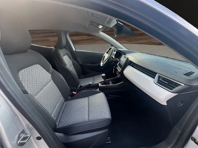 Intérieur avant de la Renault Clio V gris Highland, vue côté conducteur montrant sièges tissu gris et tableau de bord clair.