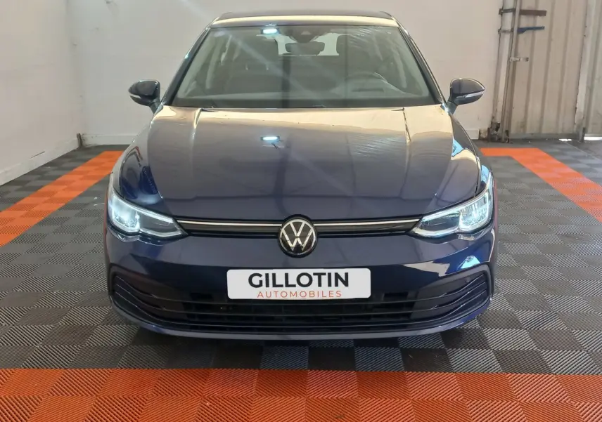 Volkswagen Golf bleu vue de face avec phares LED allumés et logo VW centré sur calandre noire.