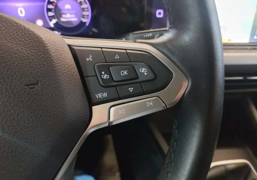 Gros plan sur les commandes multifonctions côté gauche du volant cuir de la Volkswagen Golf 2022 avec affichage digital violet en arrière-plan.