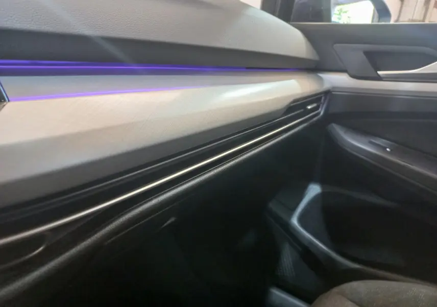 Détail du tableau de bord côté passager avec éclairage d'ambiance violet dans une Volkswagen Golf bleue 2022.