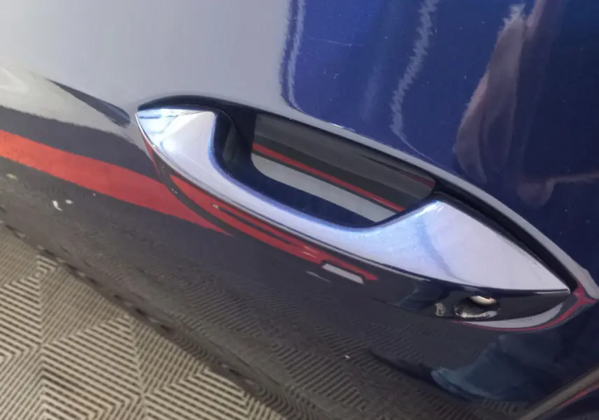 Poignée de porte avant droite bleu métallisé sur Volkswagen Golf 1.5 ETSI 2022, reflet rouge et sol texturé visible