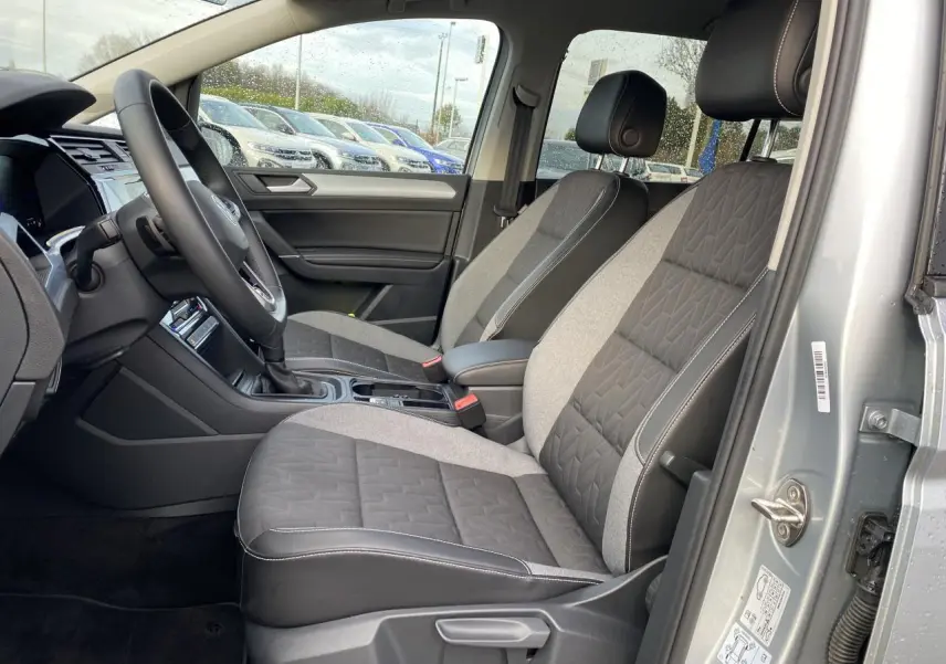 Vue intérieure côté conducteur du Volkswagen Touran 2025 en Oyster Argent métallisé, sièges tissu bicolore gris et noir.