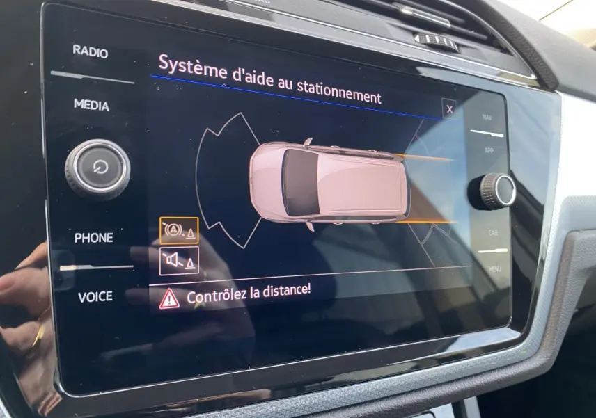 Écran tactile intérieur du Volkswagen Touran 2025 affichant le système d'aide au stationnement en vue de dessus du véhicule.