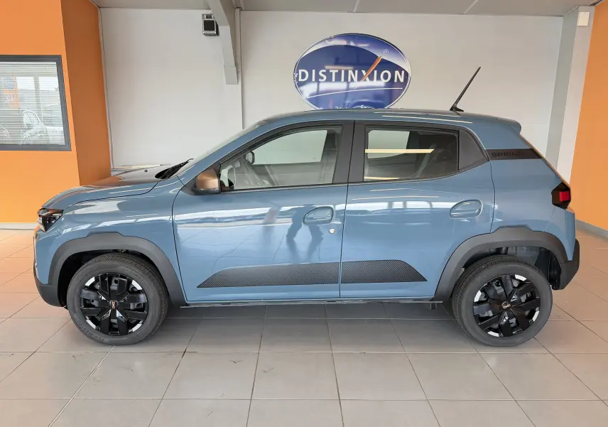 Vue de profil côté gauche d'une Dacia Spring 65 Extreme 2026 bleu ardoise avec jantes noires et détails noirs contrastants.