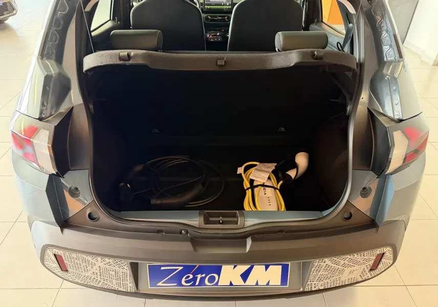 Vue arrière du Dacia Spring 65 Extreme bleu ardoise 2026 avec coffre ouvert et câbles de recharge électrique visibles.
