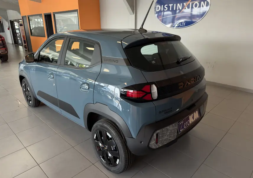 Vue 3/4 arrière droite d'une Dacia Spring 65 Extreme bleu ardoise électrique, avec jantes noires et bandeau arrière distinctif.
