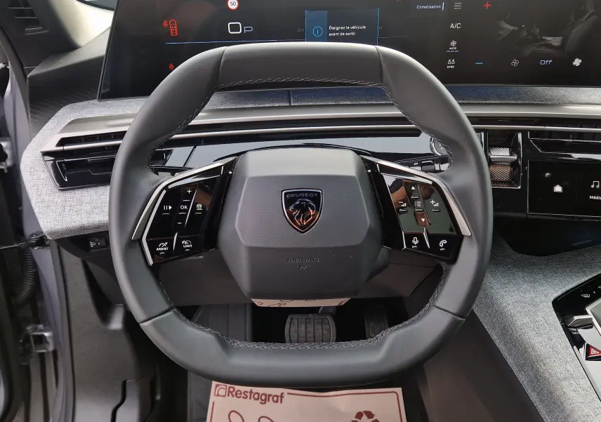 Vue intérieure centrée sur le volant cuir du Peugeot 3008 gris Artense 2025 avec écran panoramique 21 pouces en arrière-plan.
