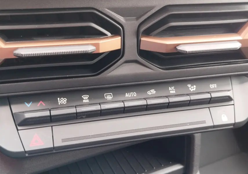 Vue rapprochée des commandes de climatisation et des aérateurs noirs avec inserts cuivrés du tableau de bord du Dacia Duster gris schiste.