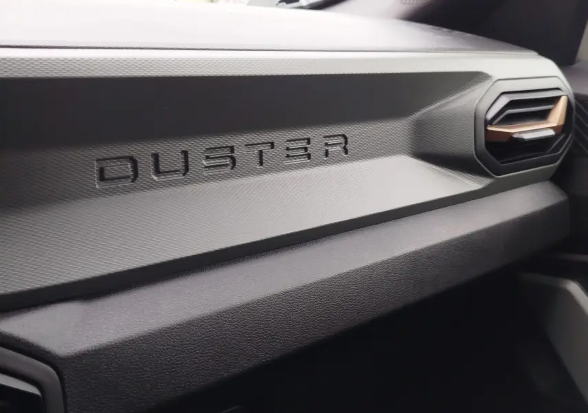Détail intérieur du tableau de bord gris avec inscription DUSTER et sortie d'air au design hexagonal.