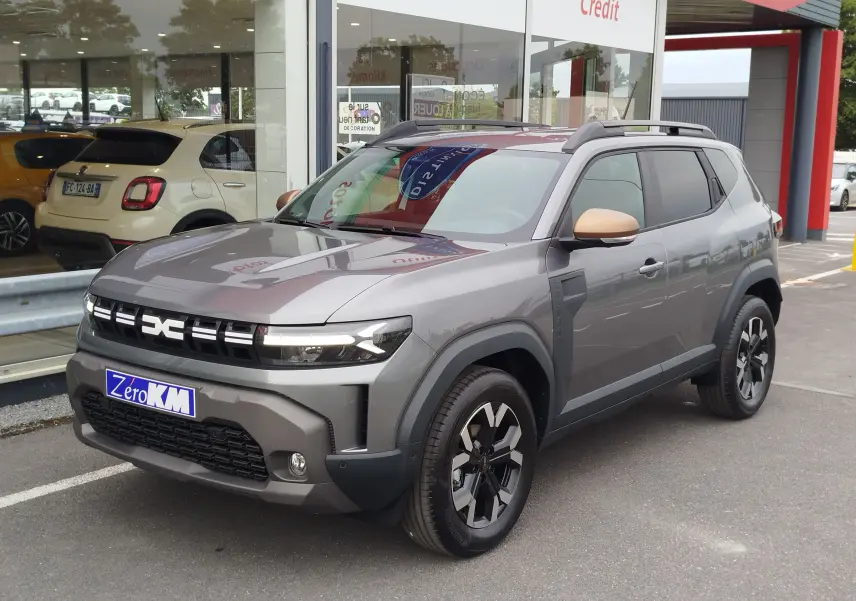 Dacia Duster gris schiste en 3/4 avant droit, avec rétroviseurs couleur cuivre et jantes noires distinctives.