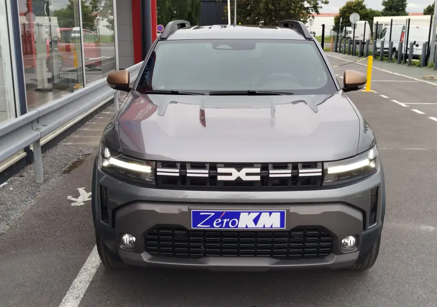Vue frontale d'un Dacia Duster gris schiste 2025 avec phares allumés et calandre noire marquée du logo Dacia.