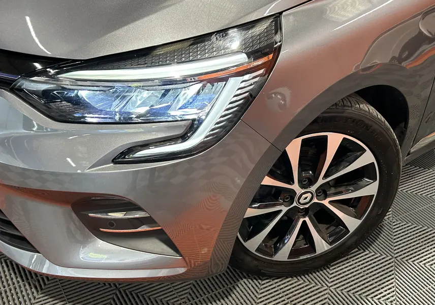 Gros plan sur l'avant droit gris métallisé de la Renault Clio V 2023, mettant en valeur son phare LED et sa jante alliage.