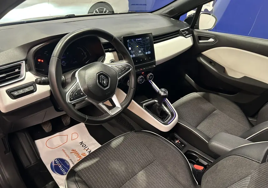 Intérieur avant droit de la Renault Clio V TCe 90 TECHNO 2023 avec tableau de bord clair et volant multifonction noir.