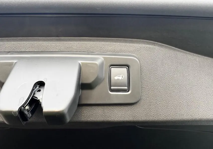 Gros plan sur le bouton d'ouverture du hayon du Renault Espace VI noir étoilé, situé sur le bord intérieur du coffre.