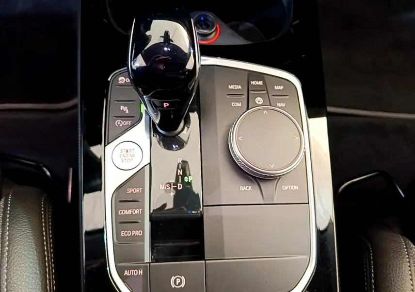 Gros plan sur la console centrale noire brillante de la BMW Série 1 118i 2021 avec levier de vitesse automatique et molette de contrôle.