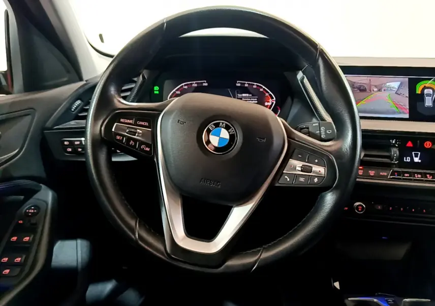 Vue rapprochée du volant cuir BMW Série 1 gris clair avec tableau de bord numérique et écran de caméra de recul.