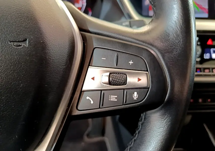 Gros plan sur les commandes du volant cuir noir de la BMW Série 1 gris clair, avec boutons multifonctions et molette argentée.