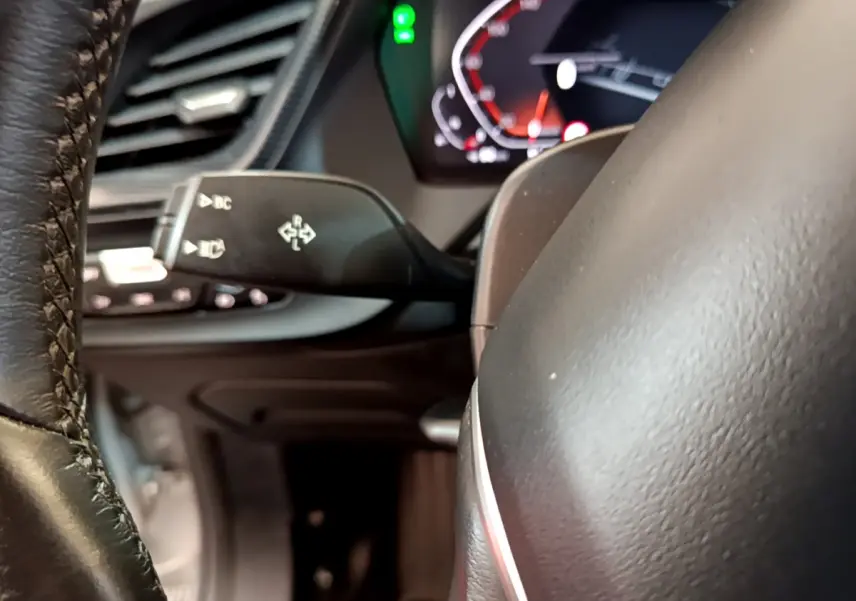 Gros plan sur le volant cuir et la commande de clignotants à gauche du tableau de bord numérique de la BMW Série 1 gris clair.