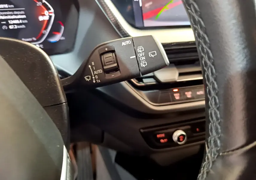 Gros plan sur la commande d'essuie-glace à gauche du volant cuir d'une BMW Série 1 gris clair, tableau de bord en arrière-plan.