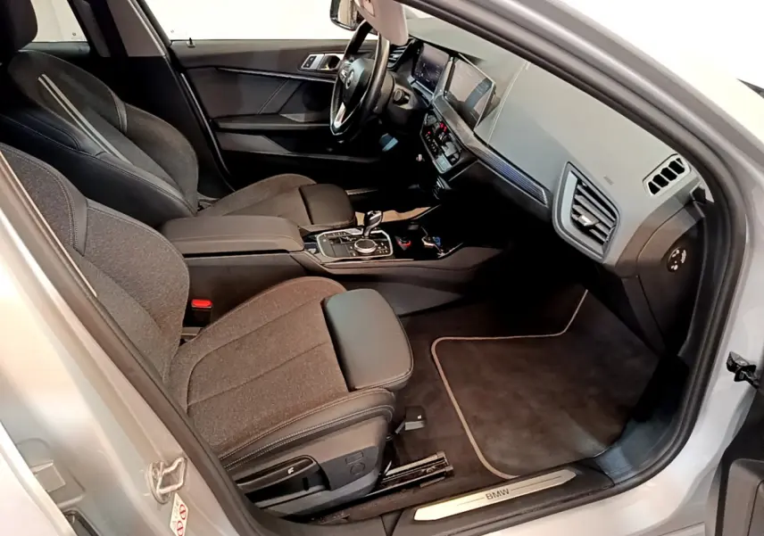 Intérieur avant droit d'une BMW Série 1 gris clair, sièges tissu et cuir, tableau de bord moderne avec écran digital.