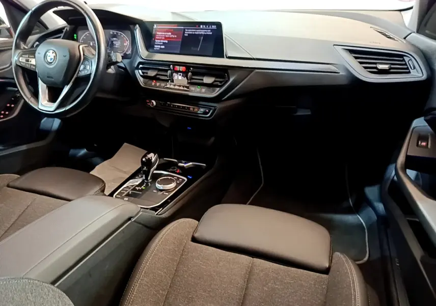 Intérieur de BMW Série 1 gris clair, vue côté conducteur sur tableau de bord, volant cuir et écran central tactile.