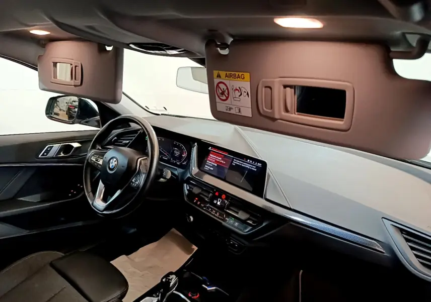 Intérieur BMW Série 1 2021 vu côté conducteur, tableau de bord noir avec écran tactile et volant cuir multifonctions.