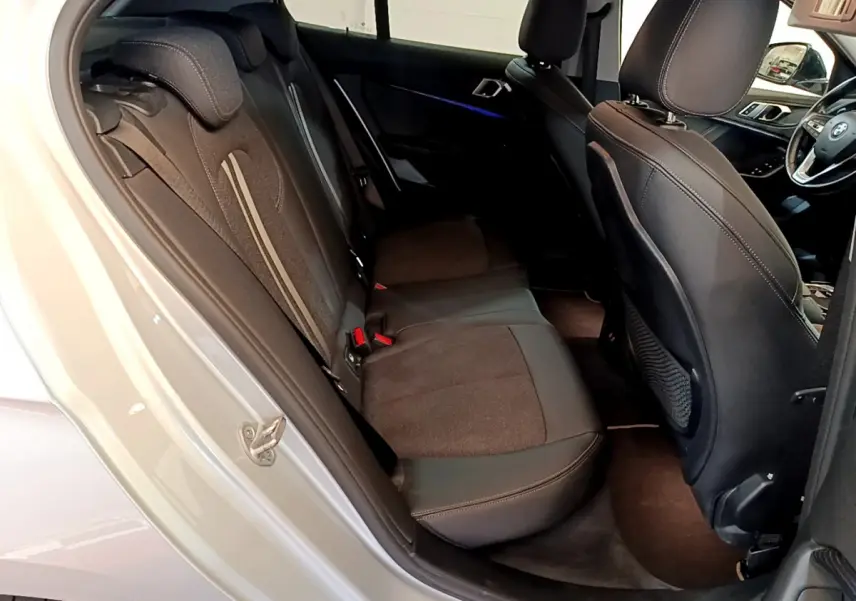 Vue intérieure côté arrière gauche de la BMW Série 1 gris clair, montrant la banquette arrière et une partie du tableau de bord.