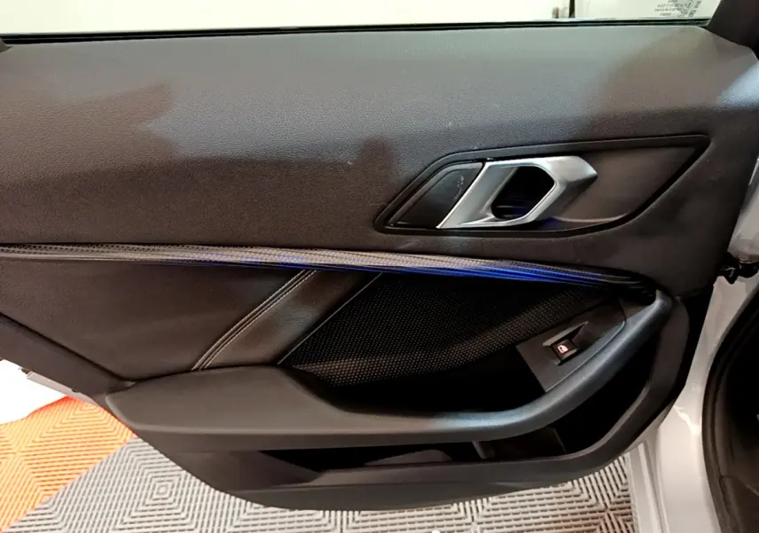 Gros plan sur la porte intérieure côté gauche d'une BMW Série 1 gris clair avec poignée alu et éclairage d'ambiance bleu