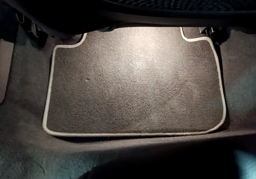 Tapis de sol gris foncé avec bordure claire, vue rapprochée de l'intérieur au niveau des pieds avant d'une BMW Série 1.