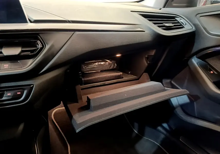 Vue intérieure côté passager du tableau de bord et boîte à gants ouverte d'une BMW Série 1 gris clair Edition Sport 2021.