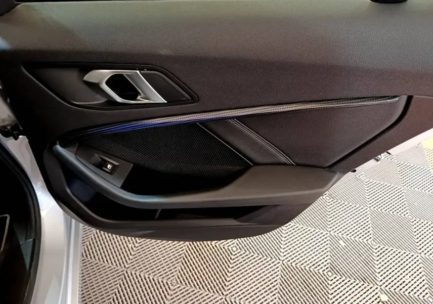 Gros plan sur la porte côté gauche d'une BMW Série 1 gris clair, mettant en valeur la poignée intérieure et les finitions noires.