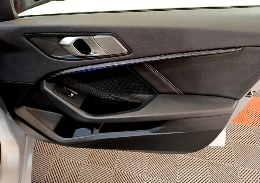 Intérieur côté gauche de la porte BMW Série 1 gris clair, avec poignée argentée et garniture noire élégante.