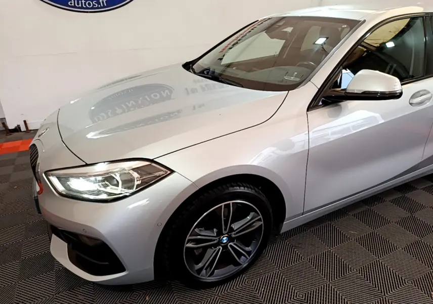 BMW Série 1 gris clair vue 3/4 avant droit avec phares LED allumés et jantes alliage sport