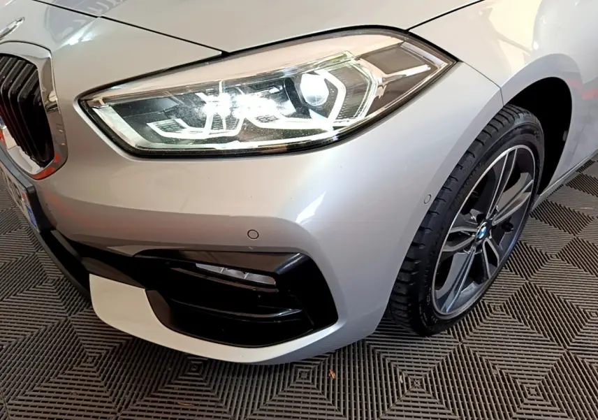 Gros plan sur l'avant droit d'une BMW Série 1 gris clair, mettant en valeur le phare LED et la jante alliage.