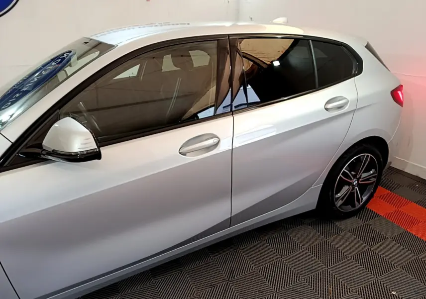 Vue latérale côté gauche d'une BMW Série 1 gris clair avec vitres teintées et jantes alliage sport.