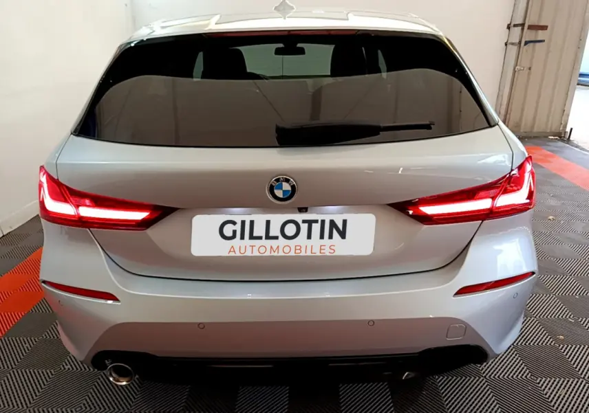 Vue arrière d'une BMW Série 1 gris clair de 2021 avec feux LED allumés et plaque GILLOTIN Automobiles.