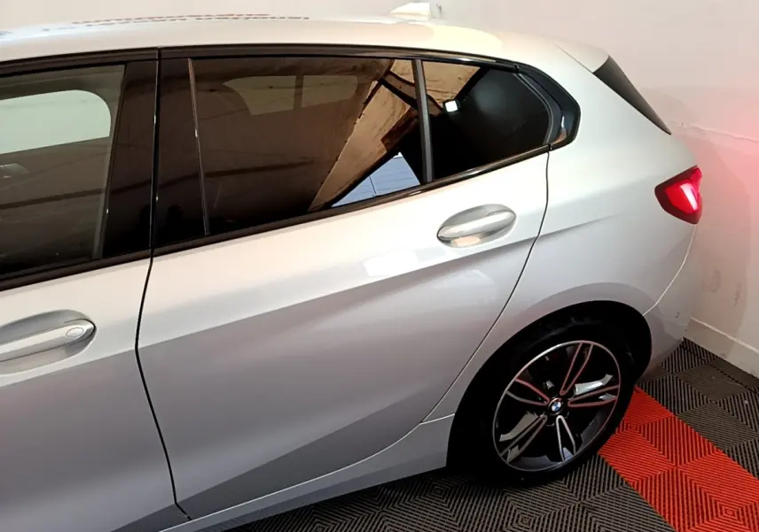 Vue côté droit arrière d'une BMW Série 1 gris clair avec jante alliage et feux arrière allumés dans un garage.